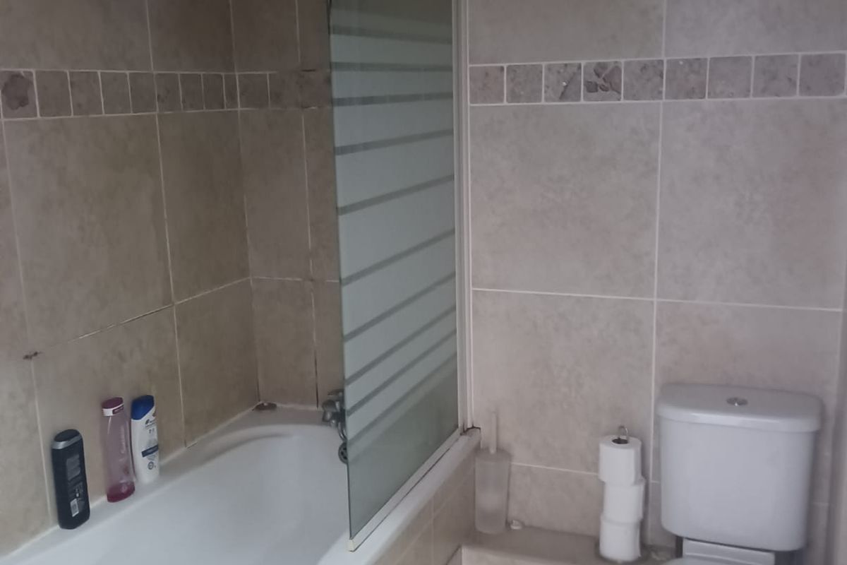 A functional bathroom featuring a built-in bathtub with a glass shower screen and a standard white toilet with tiled walls and flooring.