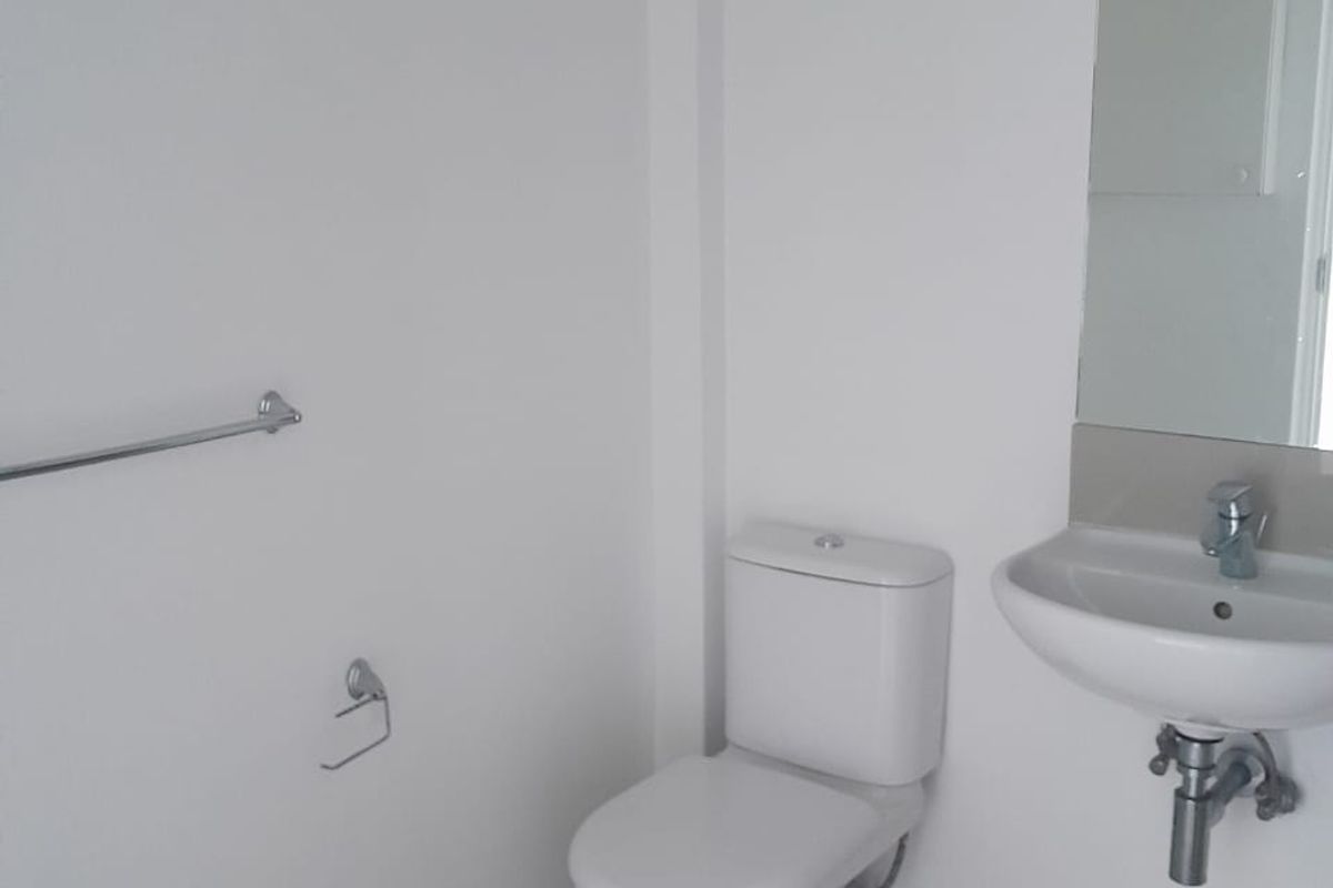 A clean and functional bathroom featuring a modern toilet, wall-mounted basin, mirror, and tiled flooring.