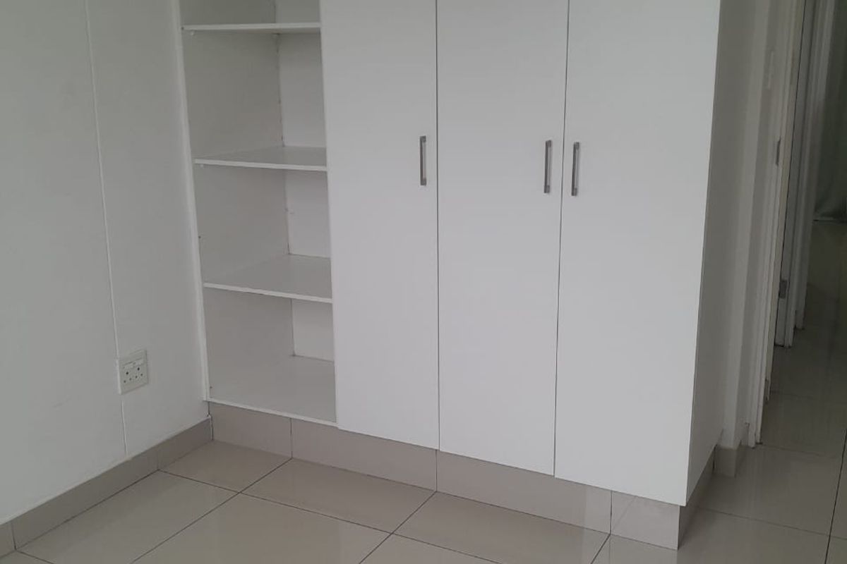 A bedroom featuring built-in white cabinetry with integrated shelving and neutral tiled flooring.