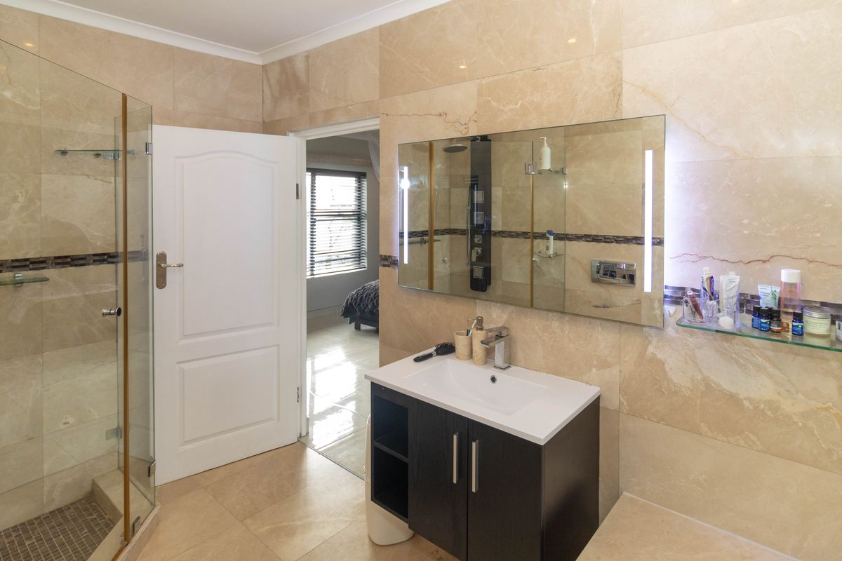 Modern bathroom featuring floor-to-ceiling marble-style tiling, a glass-enclosed shower, and a contemporary vanity with an integrated mirror and lighting.