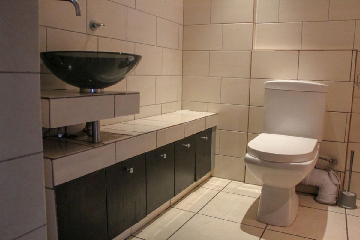 A modern bathroom featuring a dark vessel sink, built-in vanity cabinetry, and neutral wall and floor tiling.