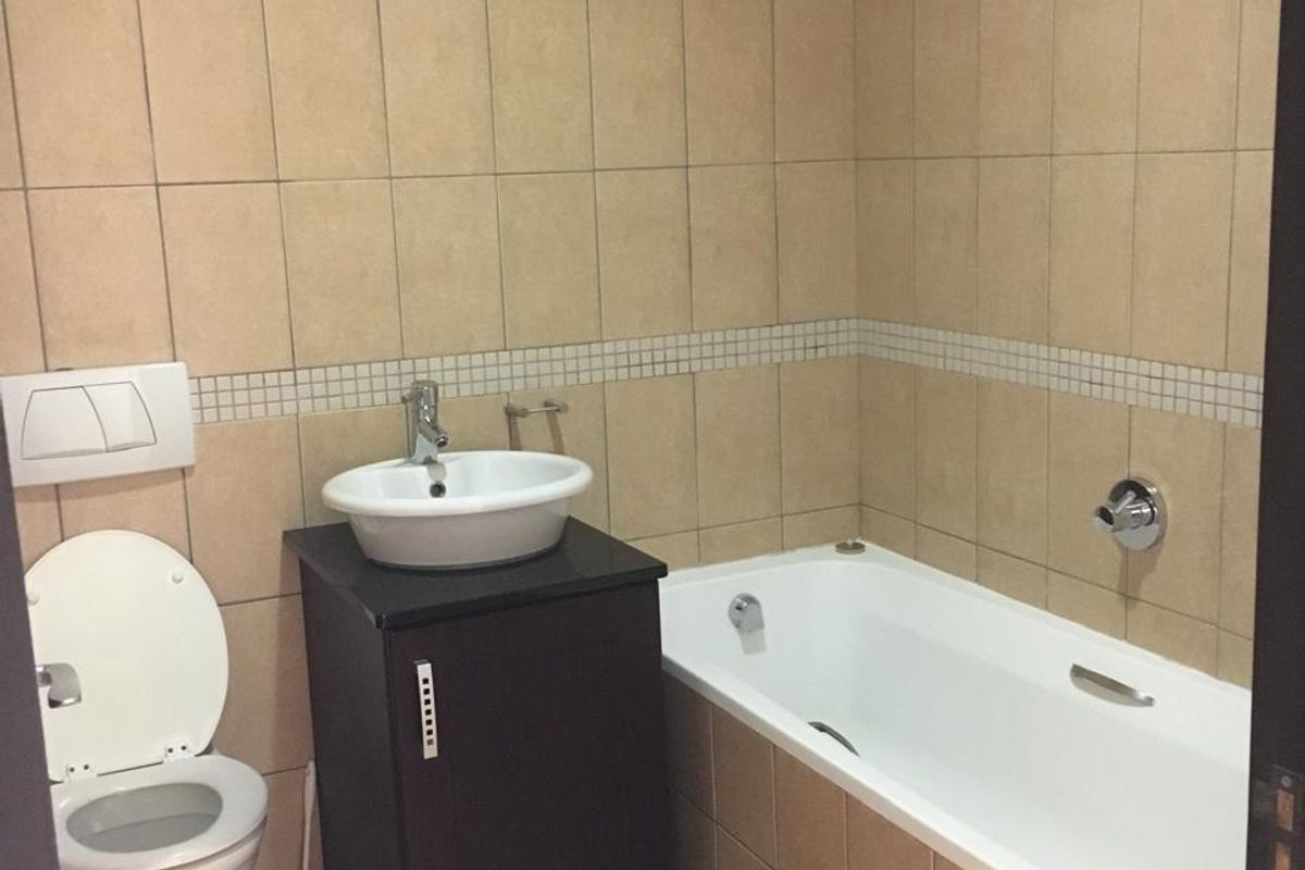 A functional bathroom featuring a wall-mounted toilet, a vanity with a vessel sink, and a tiled bathtub with chrome fixtures.