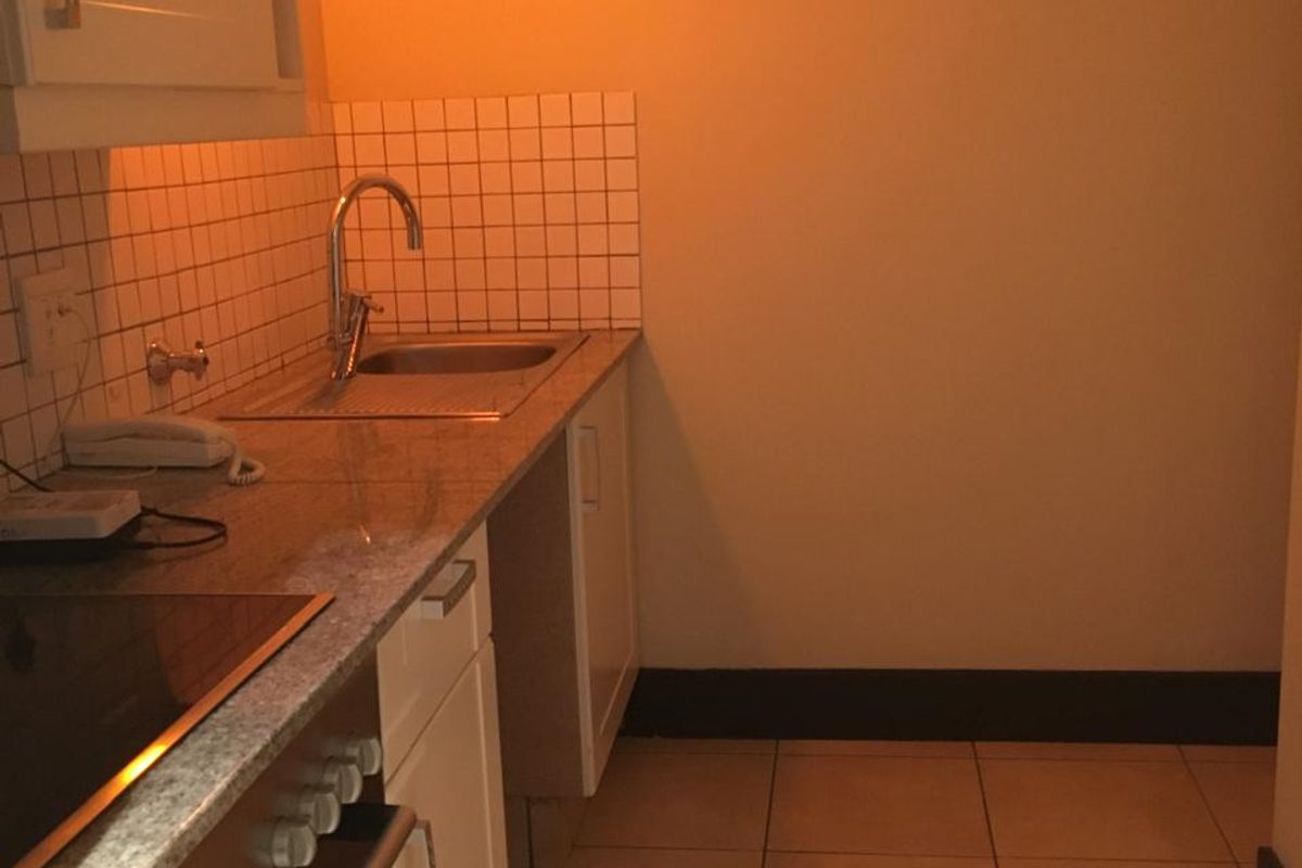 A compact kitchen featuring built-in cabinetry, a stainless steel sink, and an integrated oven with a cooktop, finished with tiled splashbacks and flooring.