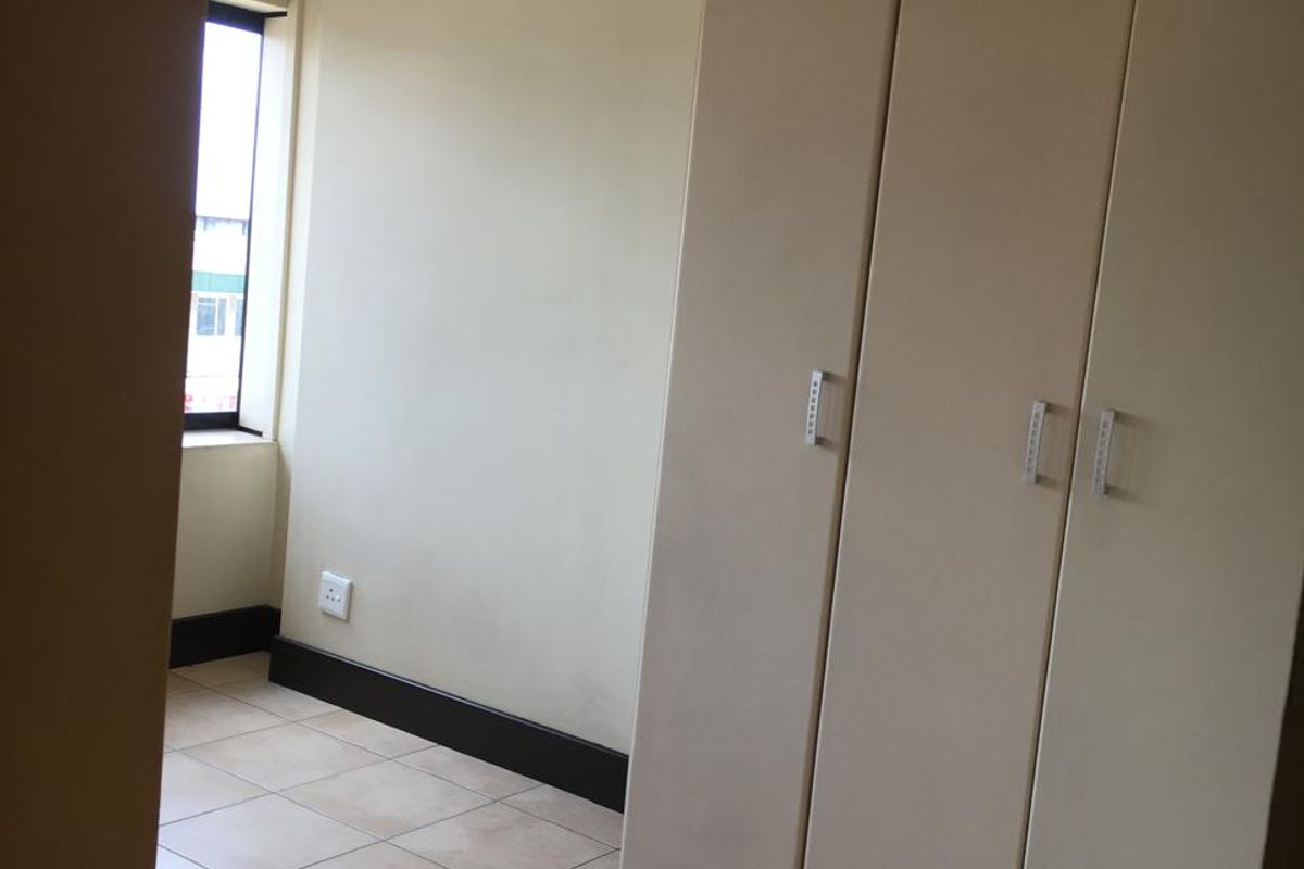 A bedroom featuring built-in cupboards, tiled flooring, and a window providing natural light.
