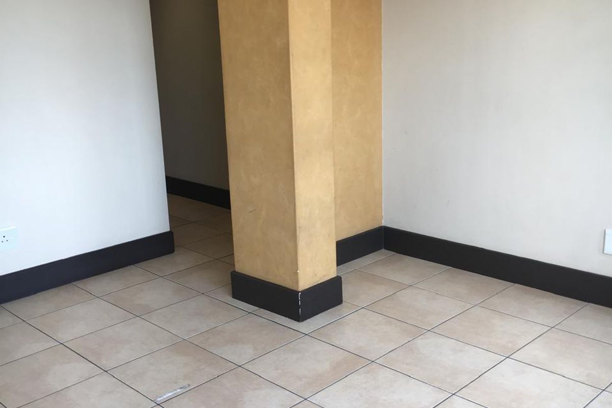 An empty interior space featuring neutral ceramic floor tiles, a central structural pillar with a textured finish, and dark contrasting skirting boards.