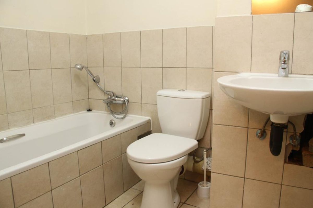 A functional bathroom featuring a bathtub, toilet, and wall-mounted basin with tiled walls, requiring minor repairs to the plumbing area under the sink.