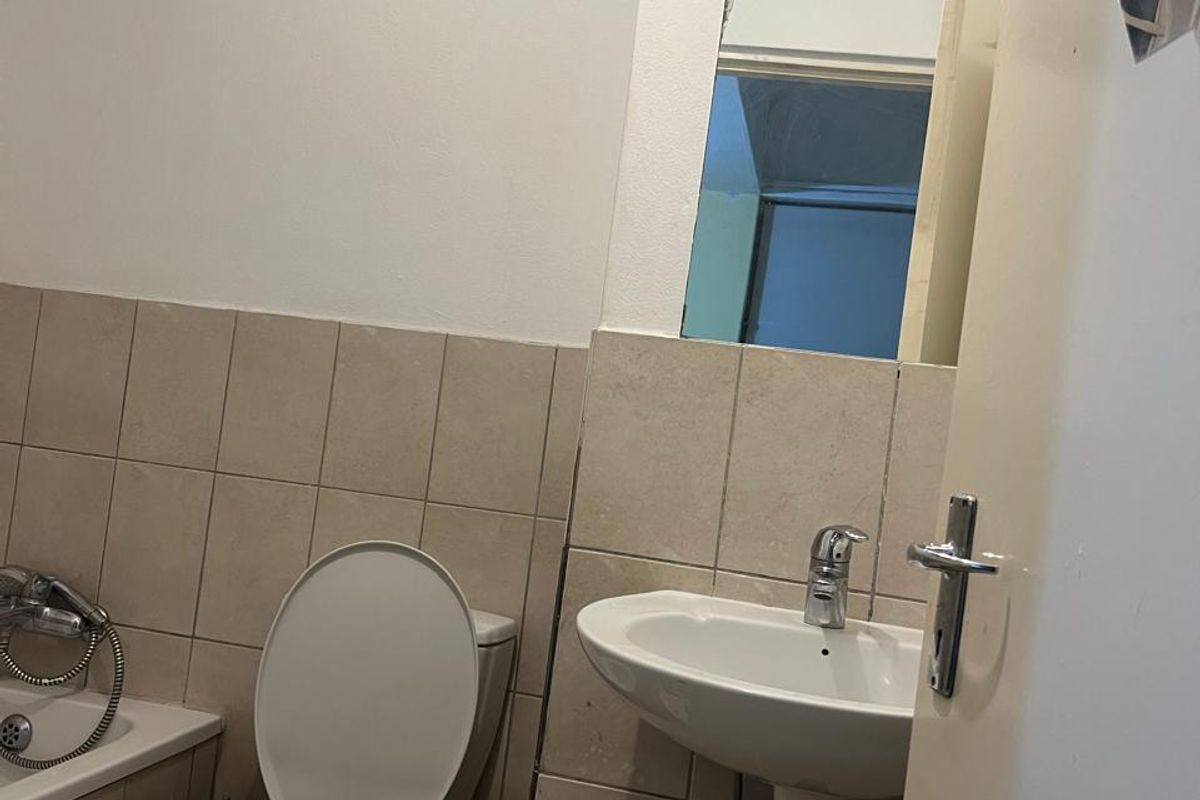 A functional bathroom featuring a wall-mounted basin, toilet, and bathtub with neutral wall tiling and a high-level window for ventilation.