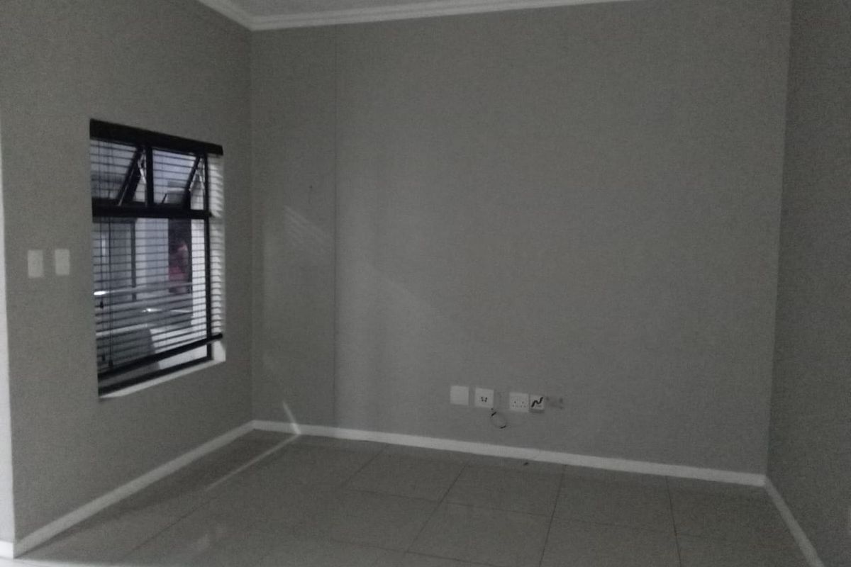 An empty bedroom featuring neutral grey walls, tiled flooring, and a window fitted with horizontal blinds.