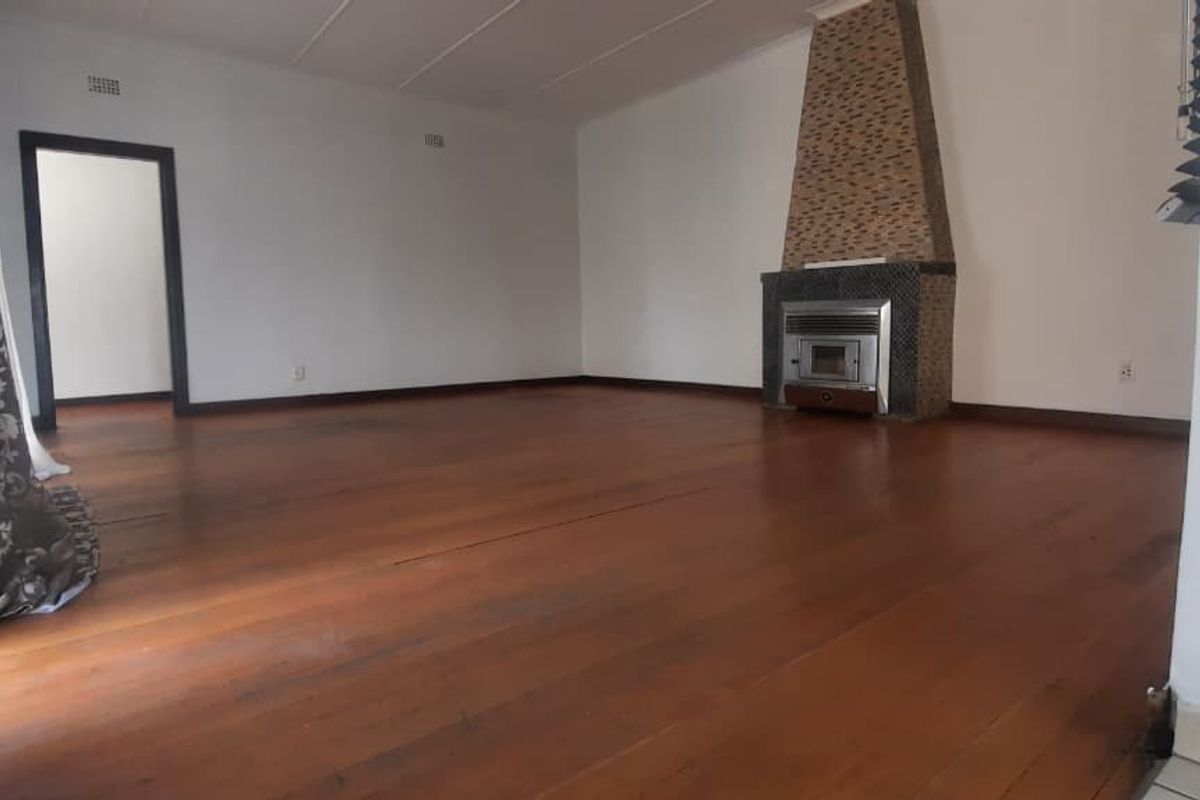 Spacious living room featuring polished timber flooring and a built-in fireplace with a decorative tiled chimney breast.