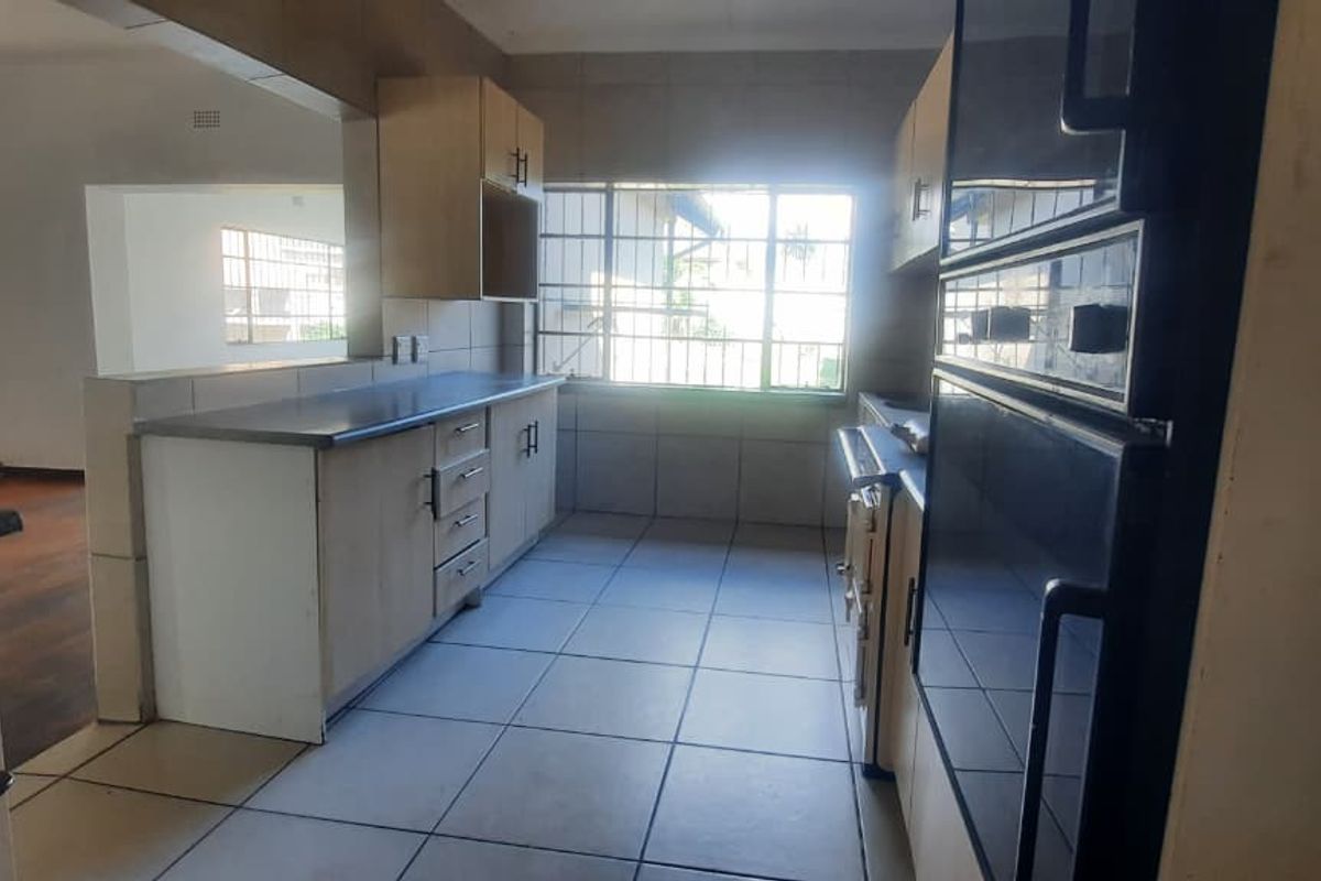 A functional kitchen featuring built-in cabinetry, a double wall oven, and tiled flooring, with an open-plan layout connecting to the adjacent living area.