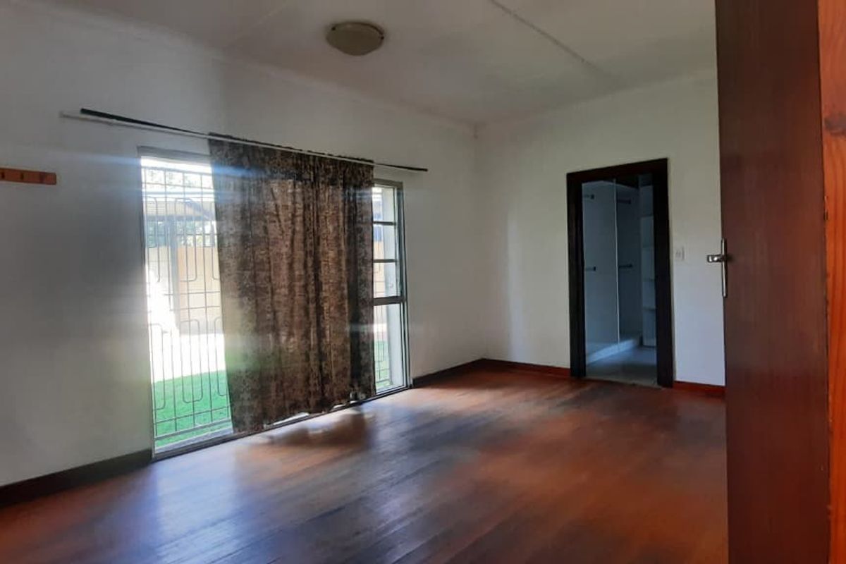 A spacious bedroom featuring polished wooden flooring, a large sliding glass door with security bars, and an adjacent walk-in closet area.