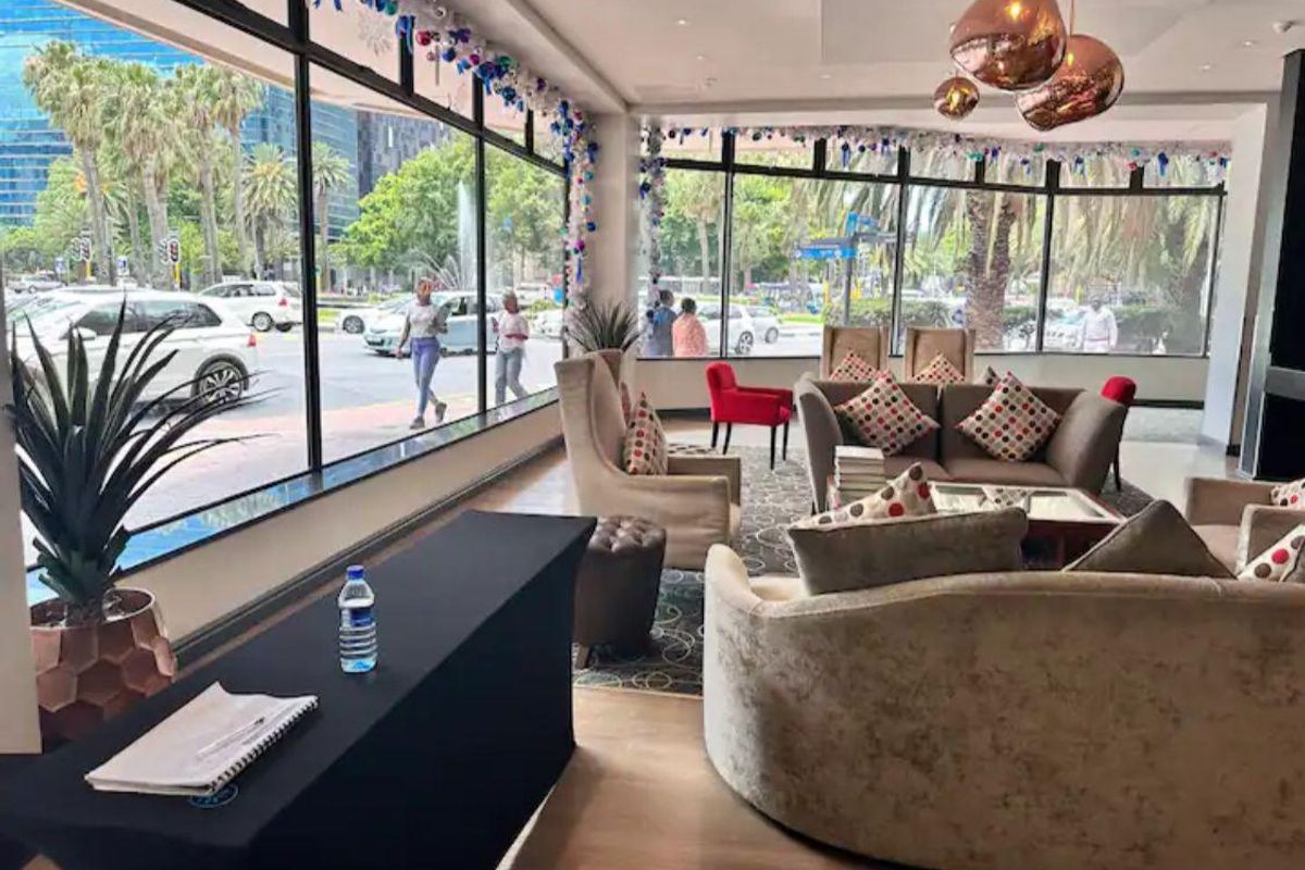 A bright, modern lobby or lounge area featuring floor-to-ceiling windows with urban views and contemporary pendant lighting.