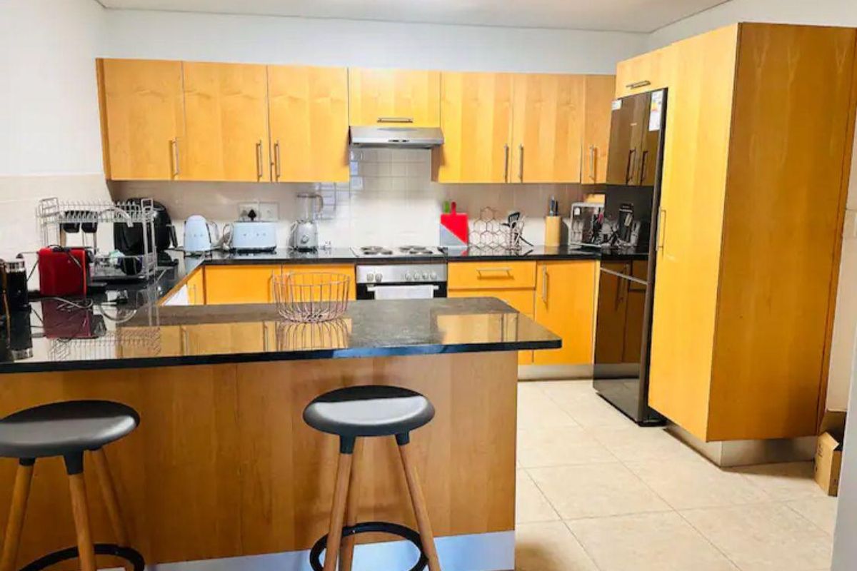 A functional kitchen featuring light wood cabinetry, black granite countertops, a breakfast bar, and integrated stainless steel appliances.
