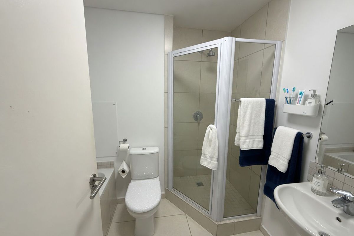 A clean and functional bathroom featuring a corner glass shower enclosure, a white ceramic toilet, and a wall-mounted vanity basin.