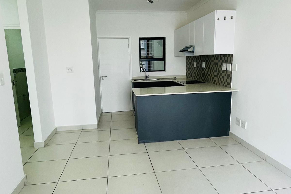 A clean, modern open-plan kitchen featuring white cabinetry, a dark breakfast bar, tiled flooring, and a built-in extractor fan.