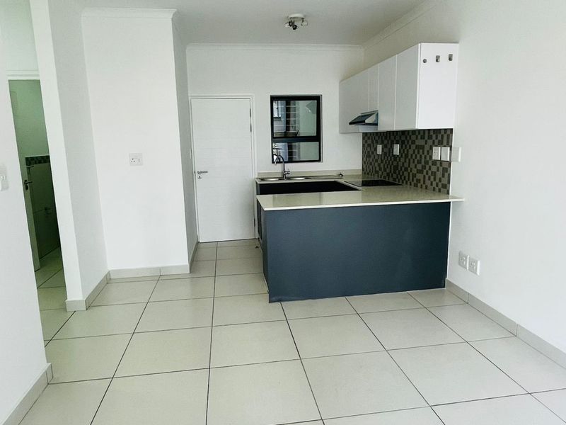 A clean, modern open-plan kitchen featuring white cabinetry, a dark breakfast bar, tiled flooring, and a built-in extractor fan.