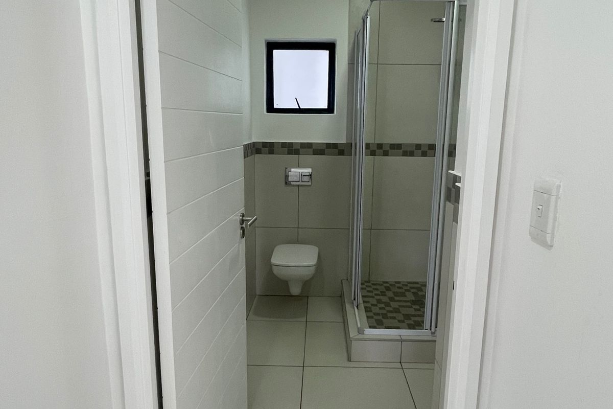 A clean, modern bathroom featuring a glass-enclosed shower, wall-mounted toilet, and neutral floor tiling.