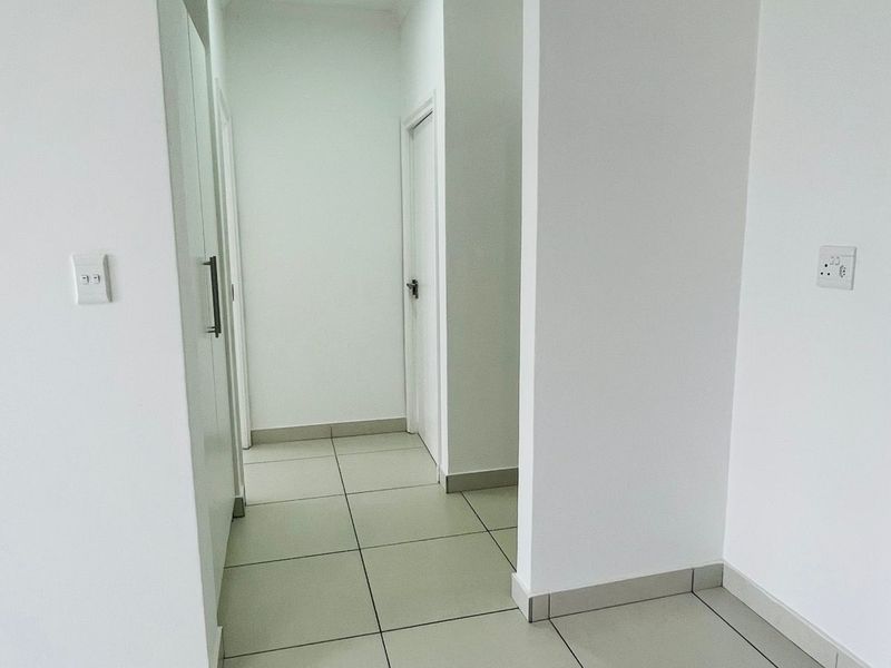 A clean, neutral hallway featuring light-colored floor tiles, built-in cabinetry, and recessed ceiling lighting, providing a bright and functional transition space.