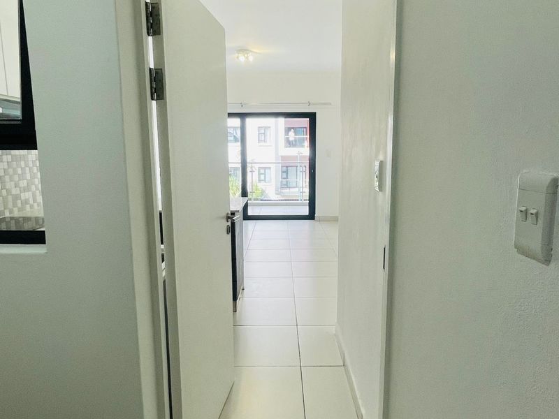 A view through a doorway into an open-plan living area with tiled flooring, leading towards a balcony with sliding glass doors.