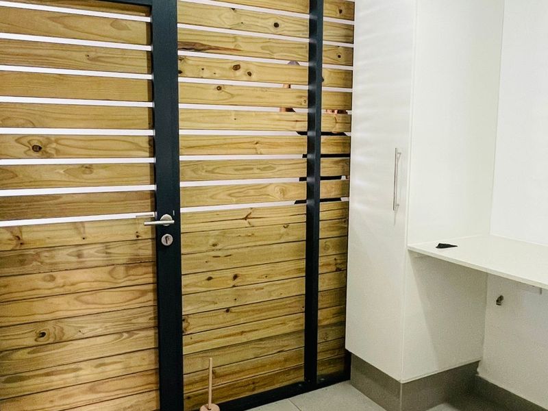 A functional laundry area featuring a slatted timber privacy screen, tiled flooring, and a built-in white cabinetry unit with a countertop.