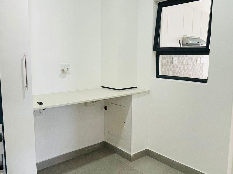 A clean and functional laundry area featuring tiled flooring, a built-in countertop, and a floor drain for utility convenience.