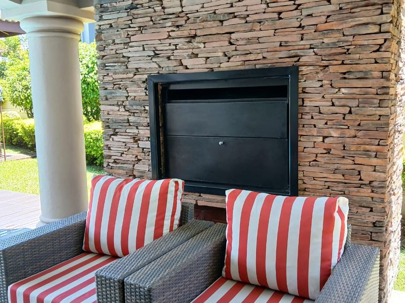 A covered patio area featuring a prominent natural stone feature wall with a built-in fireplace and classic architectural columns.