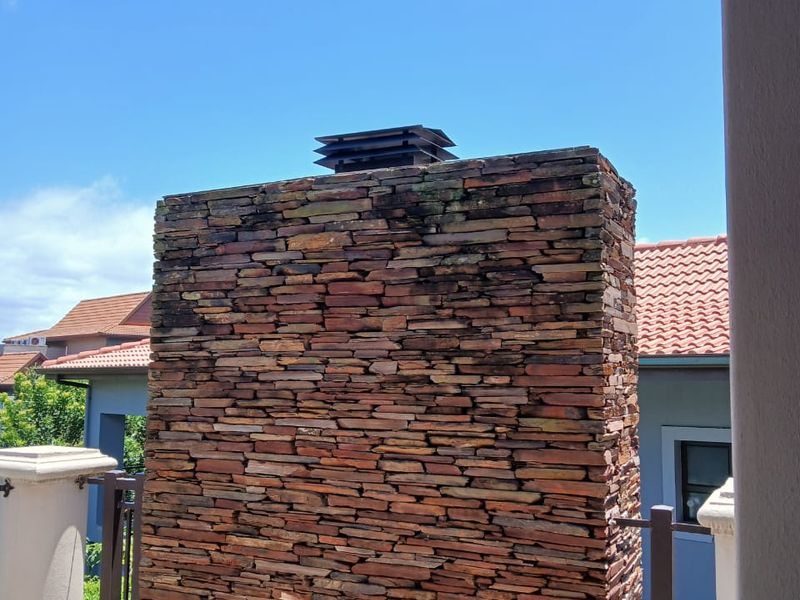 A view of a stone-clad chimney stack on an outdoor patio area, featuring tiled flooring and metal railings.