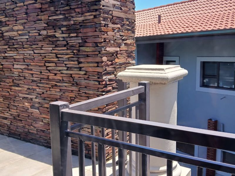 A view from an elevated balcony featuring a prominent natural stone chimney stack, metal railings, and a decorative pillar overlooking the property exterior.