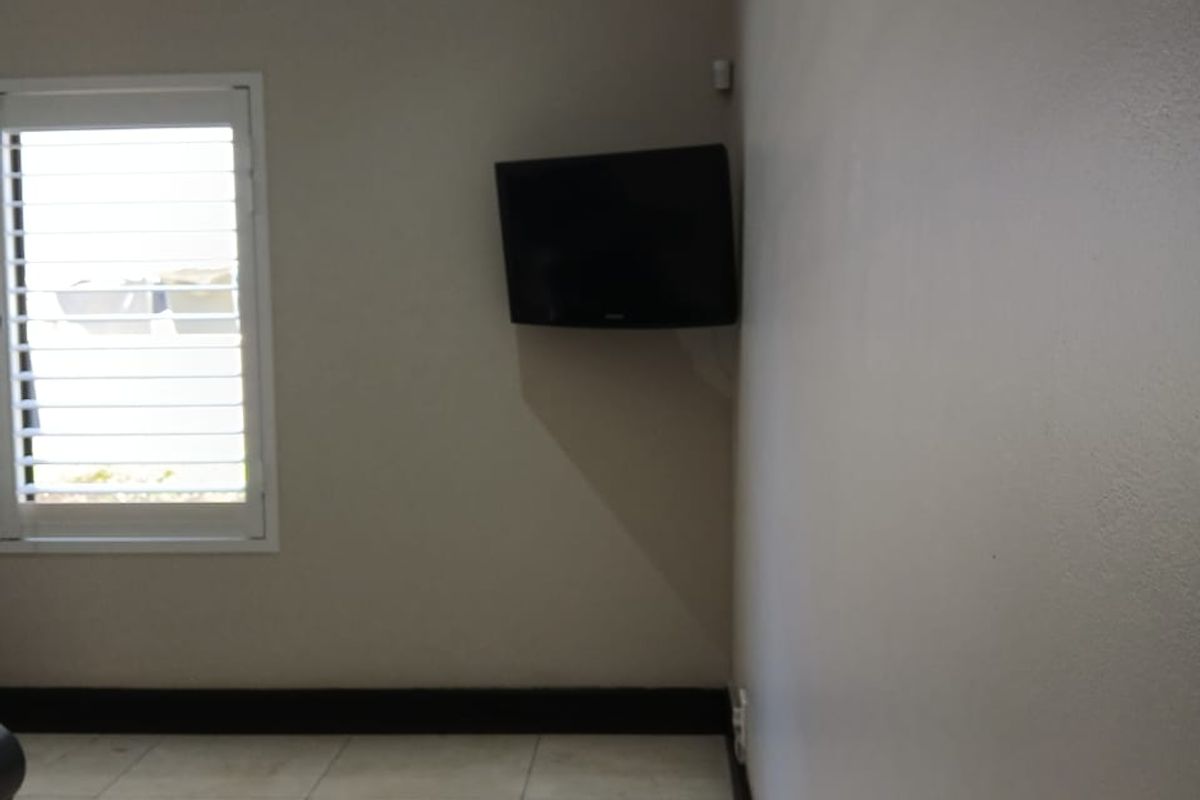 A minimalist living area featuring neutral wall tones, polished floor tiles, and plantation-style window shutters.