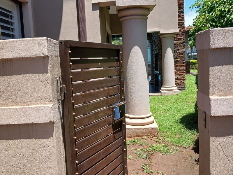 A side entrance featuring a metal gate, stone-clad feature wall, and classical-style columns leading to the rear garden area.