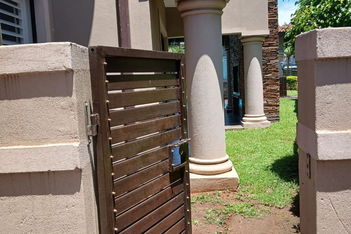 A side entrance featuring a metal gate, stone-clad feature wall, and classical-style columns leading to the rear garden area.