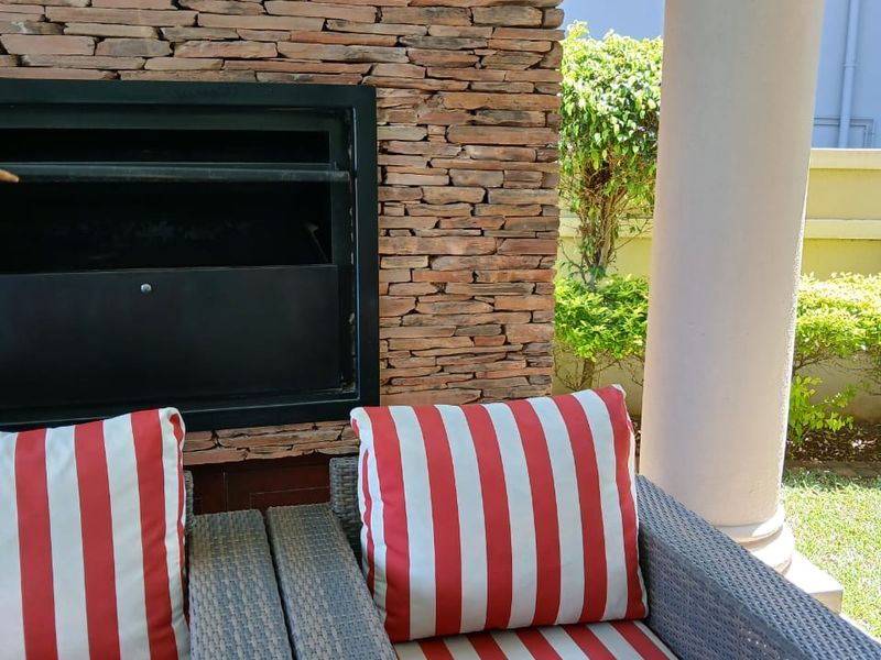 Covered patio area featuring a built-in stone fireplace and a structural column, overlooking a landscaped garden.