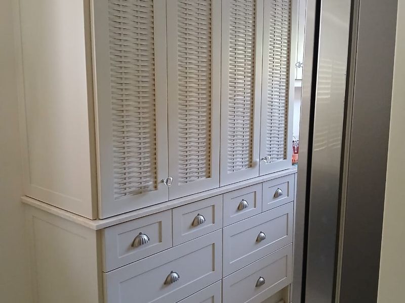 A well-maintained kitchen storage unit featuring custom cabinetry with woven-style door panels, integrated drawers, and stone countertops.