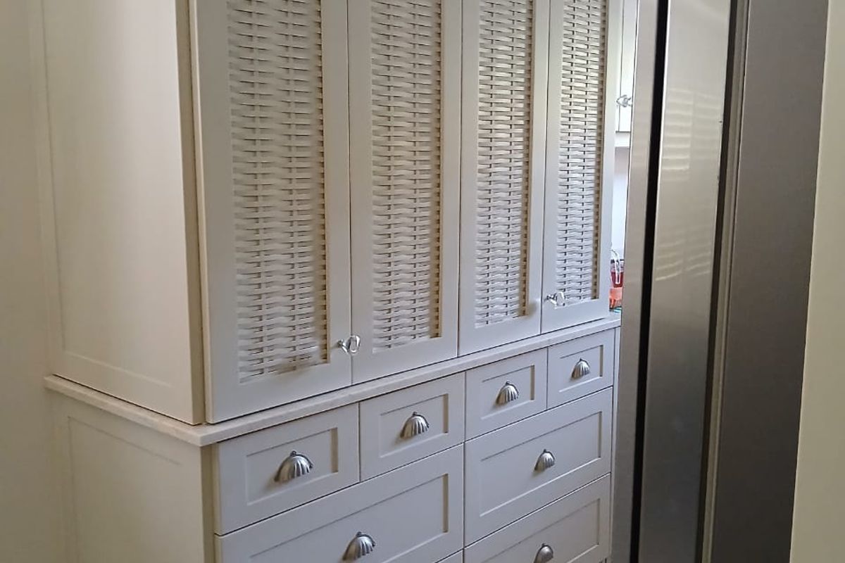 A well-maintained kitchen storage unit featuring custom cabinetry with woven-style door panels, integrated drawers, and stone countertops.