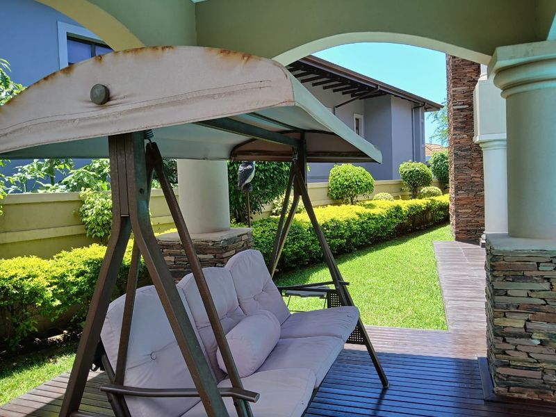 A covered patio area featuring stone-clad pillars, wooden decking, and a view of the landscaped garden and rear exterior of the house.