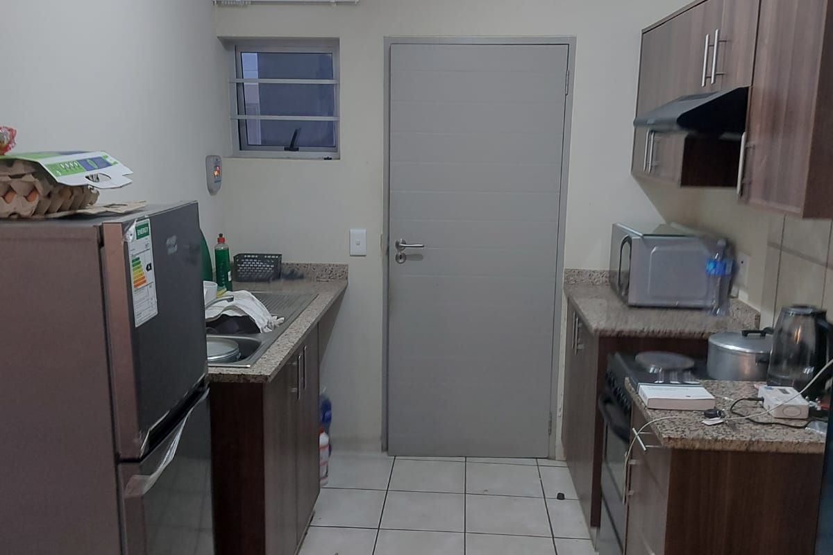 A functional galley-style kitchen featuring wood-finish cabinetry, granite countertops, a built-in stove with extractor fan, and tiled flooring.