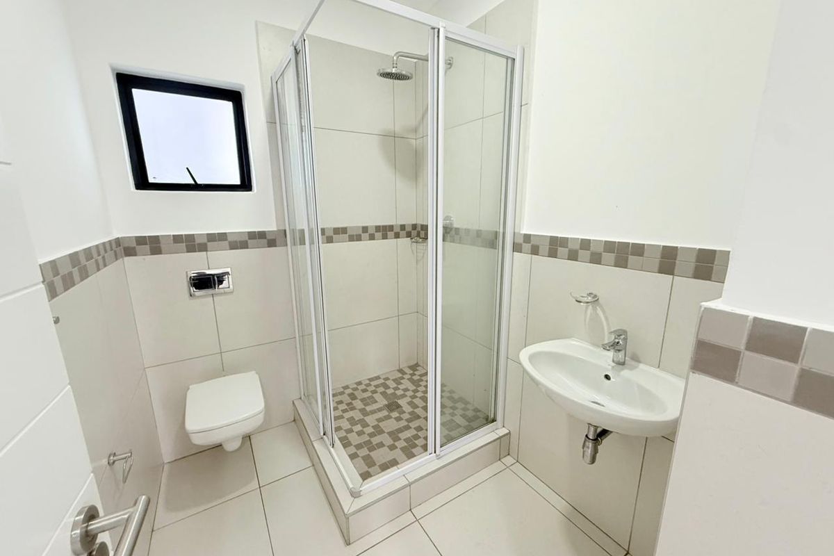 A modern, clean bathroom featuring a glass-enclosed shower, wall-mounted toilet, and a sleek pedestal basin with neutral tiled finishes.