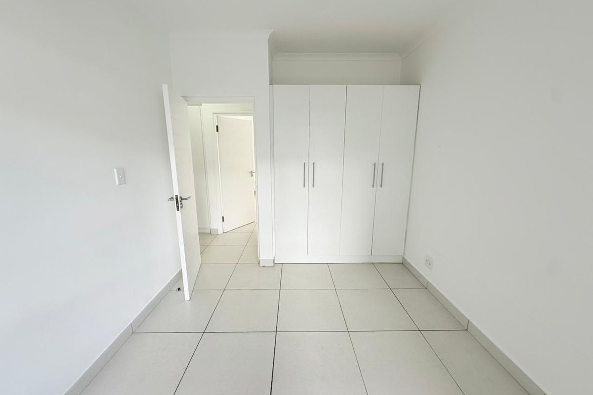A bright, empty bedroom featuring neutral floor tiles and built-in white cabinetry, offering a clean and versatile space.