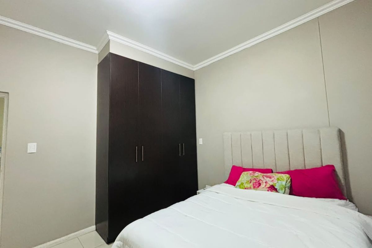 A well-maintained bedroom featuring neutral wall tones, crown molding, and a large built-in dark wood wardrobe providing ample storage space.