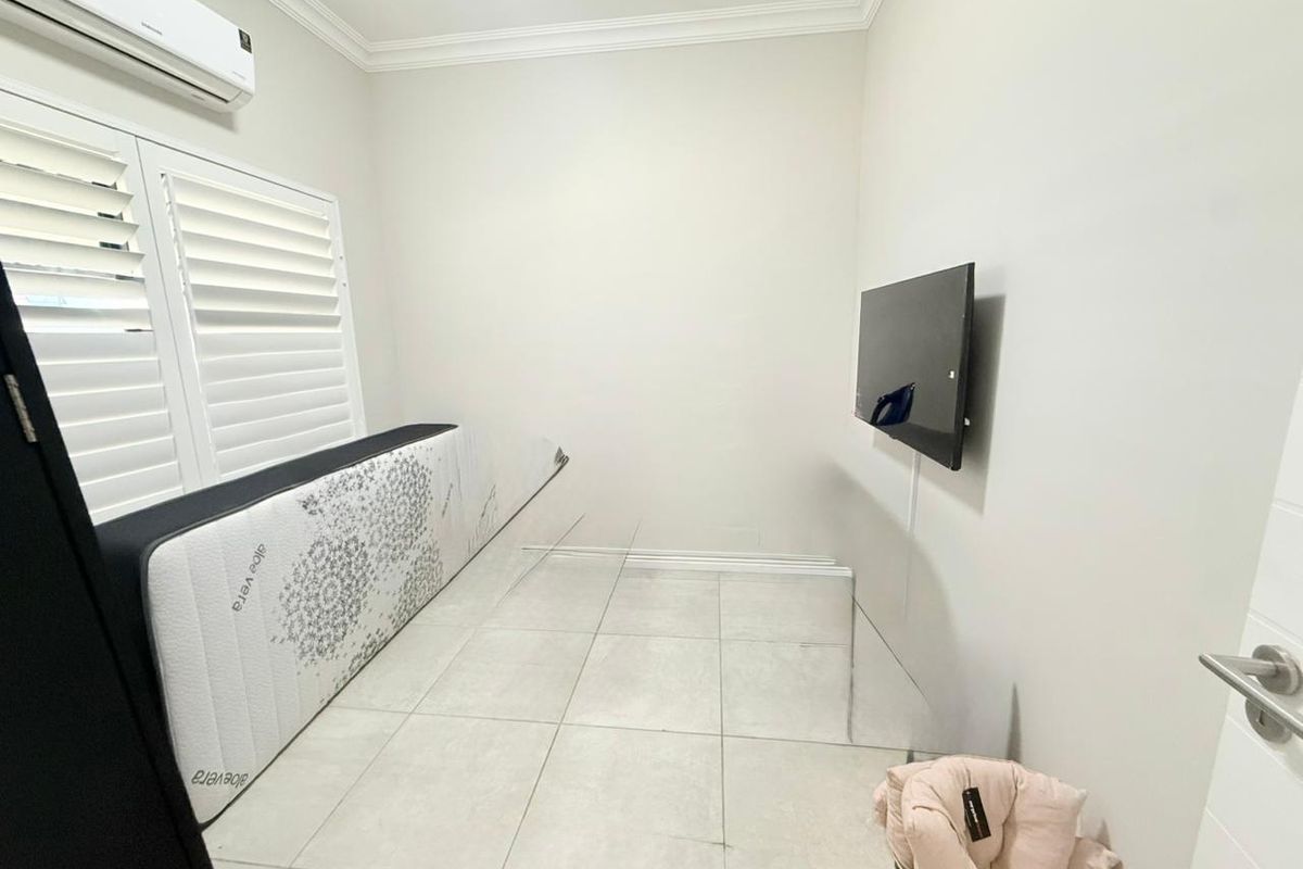 A bright bedroom featuring tiled flooring, white plantation shutters, crown molding, and a wall-mounted air conditioning unit.