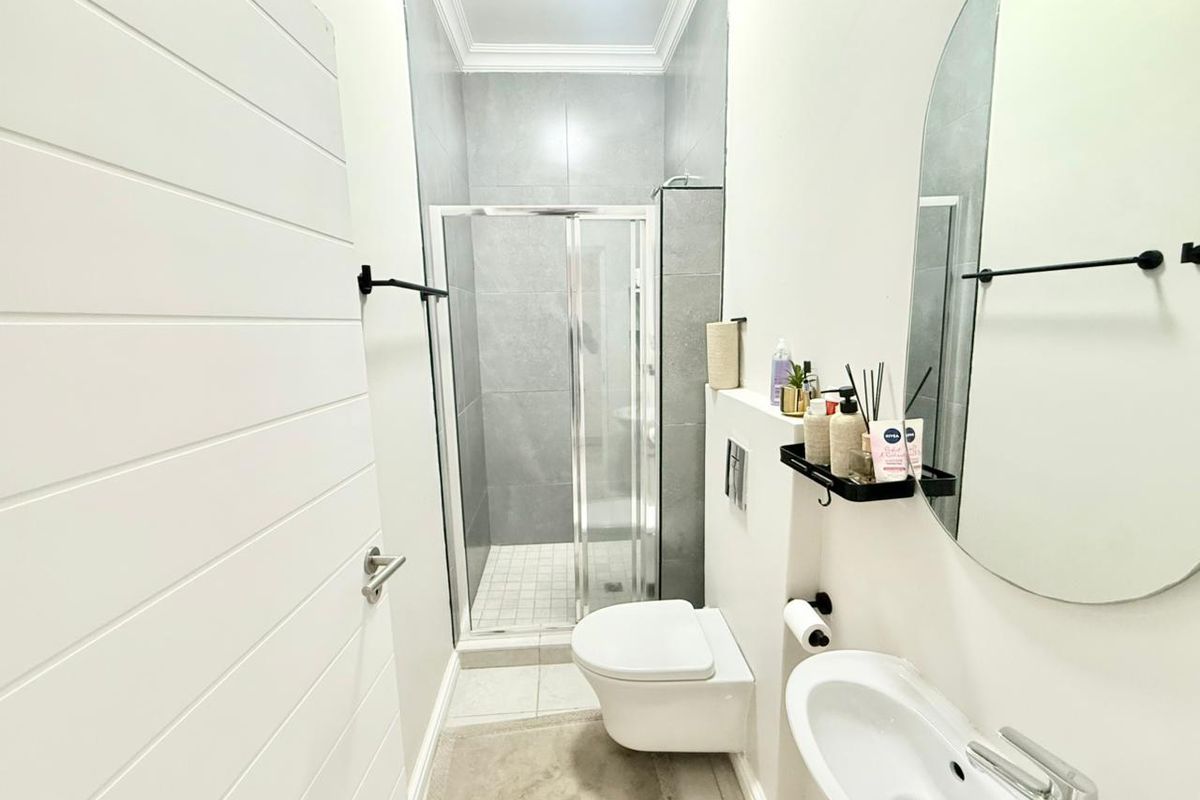 Modern bathroom featuring a walk-in shower with grey tiling, wall-mounted toilet, and a sleek vanity basin with a circular mirror.