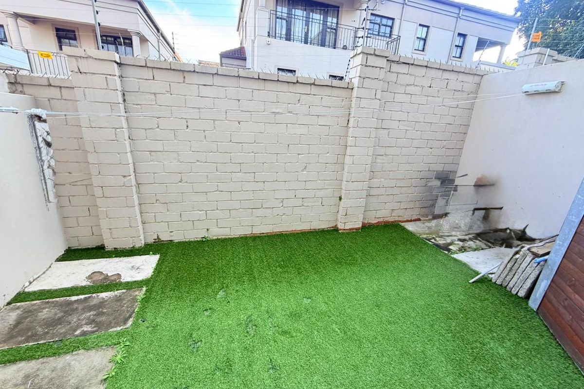 A compact rear courtyard featuring a high perimeter boundary wall, artificial grass lawn, and concrete paving sections.