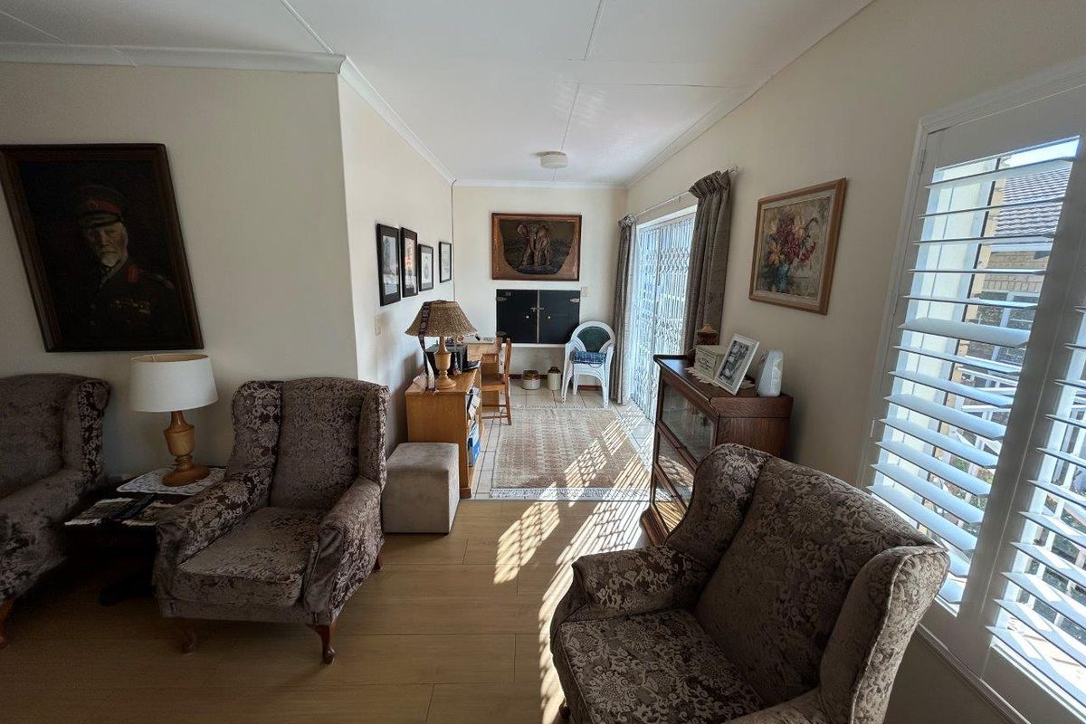 A sunlit living room featuring laminate flooring, plantation shutters, and a sliding glass door providing access to the outdoor area.