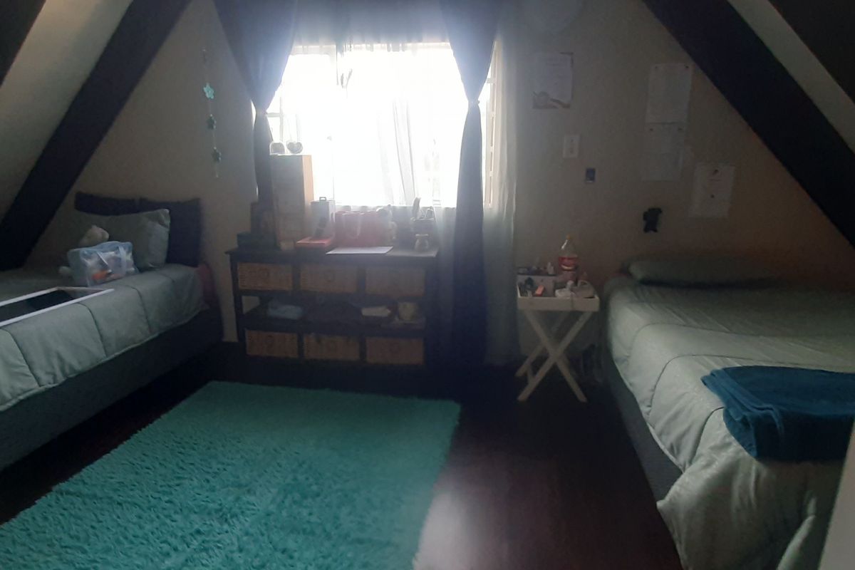Attic-style bedroom featuring exposed timber beams, sloped ceilings, and laminate flooring, providing a cozy and unique living space.