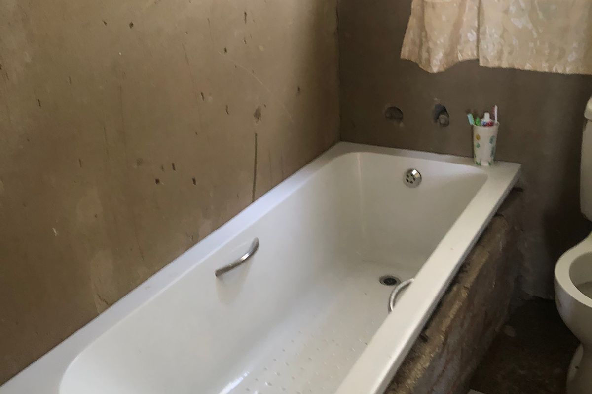 A bathroom featuring a built-in bathtub and toilet, currently requiring significant wall finishing and renovation to complete the space.