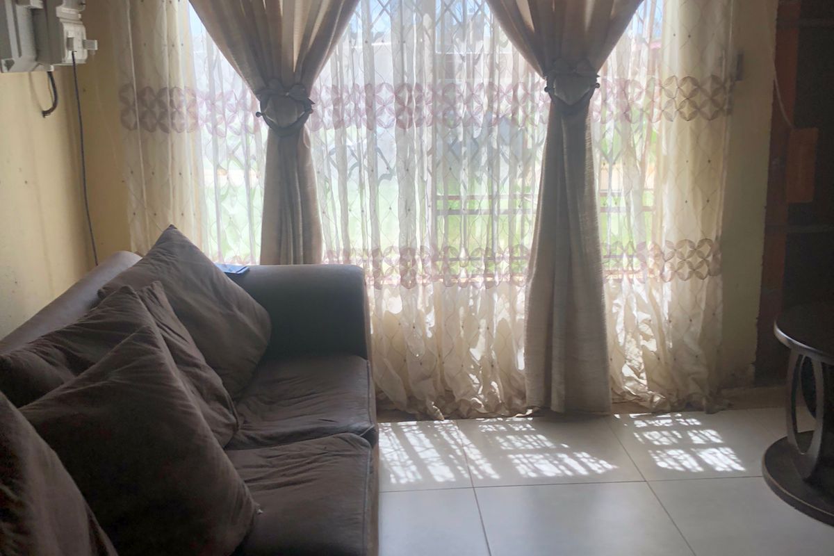 A living room featuring tiled flooring and a large window with security gate, providing natural light to the space.