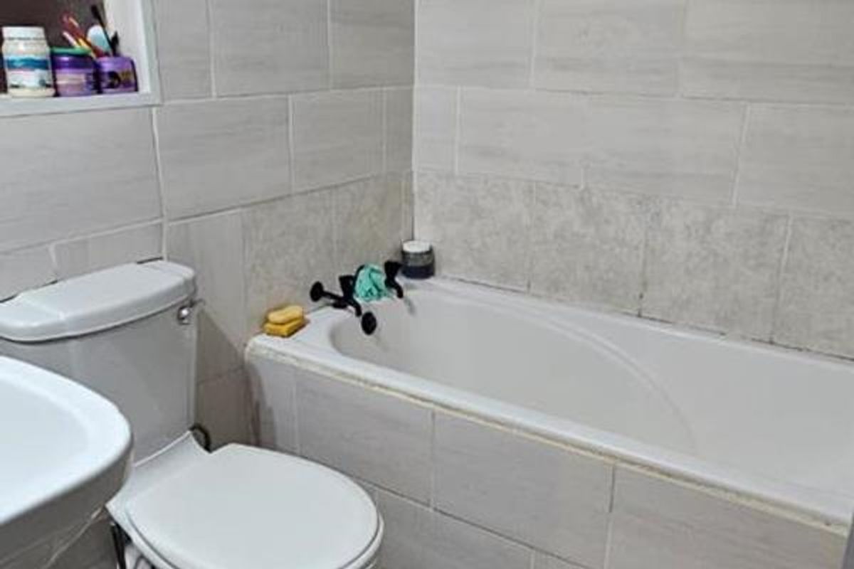 A functional bathroom featuring a standard bathtub with wall-mounted mixer taps, a white ceramic toilet, and neutral wall tiling.