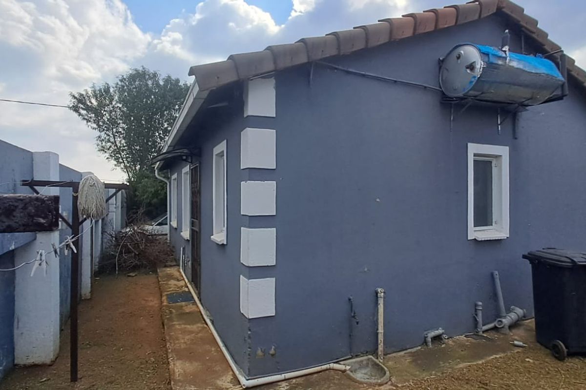 Rear view of the property featuring a solar geyser, concrete boundary wall, and side access path.