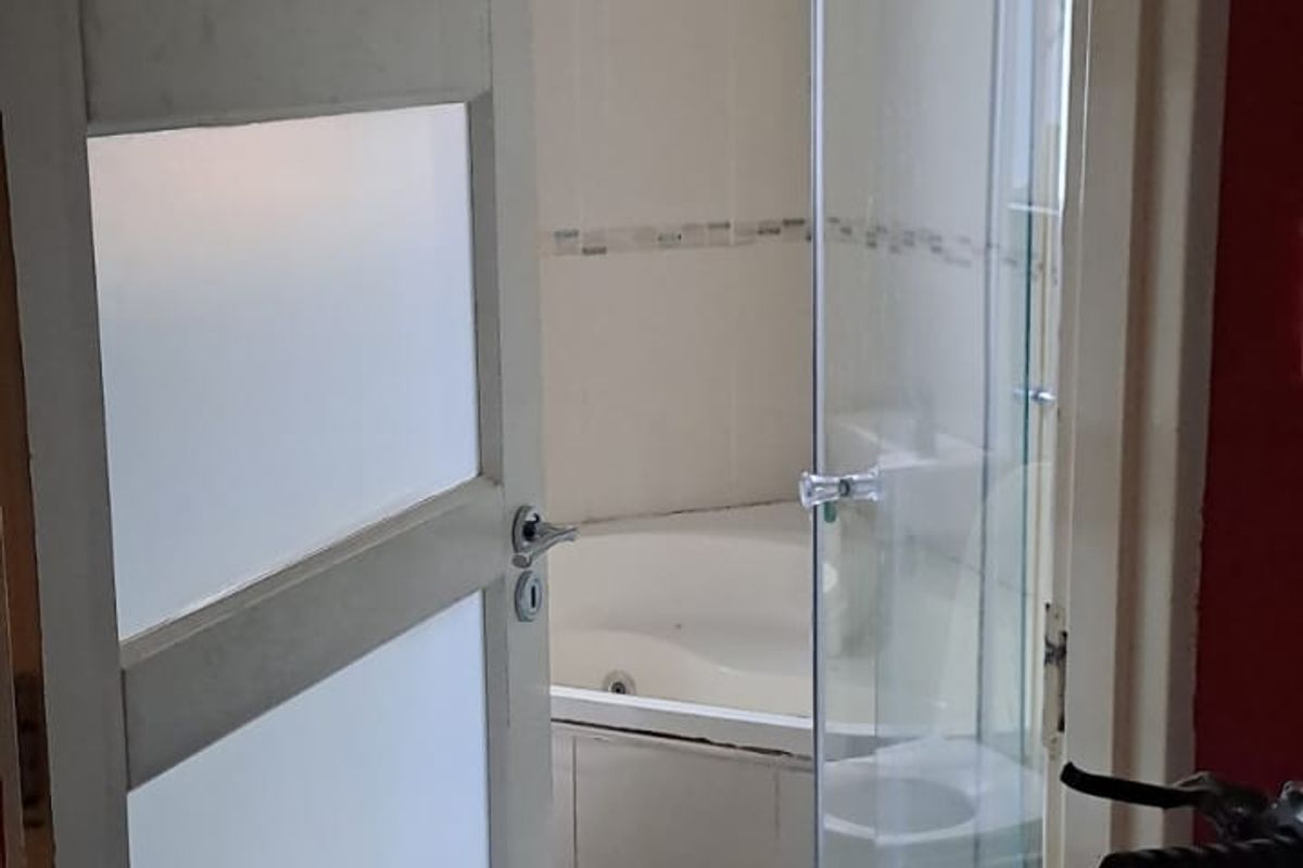 A view into a bathroom featuring a corner bathtub and a glass-enclosed shower stall, accessed through a frosted glass panel door.
