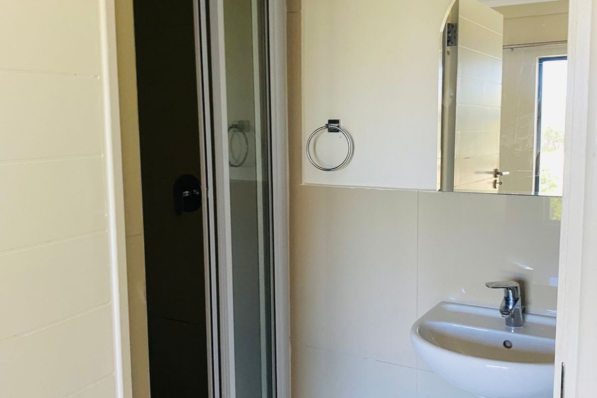 A compact bathroom featuring a wall-mounted basin, a shower enclosure with a sliding door, and a semi-circular wall mirror.
